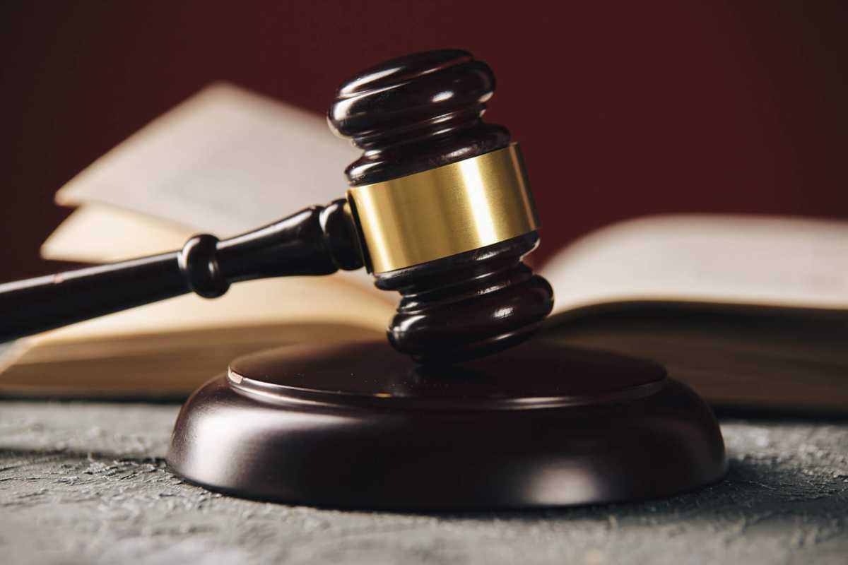 Law concept – Open law book with a wooden judges gavel on table in a courtroom or law enforcement office on blue background.