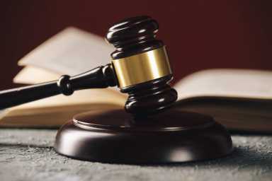 Law concept – Open law book with a wooden judges gavel on table in a courtroom or law enforcement office on blue background.