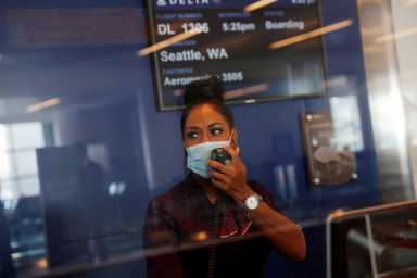 A Delta Air Lines gate agent makes an announcement for air travelers behind a protective window at JFK International Airport in New York