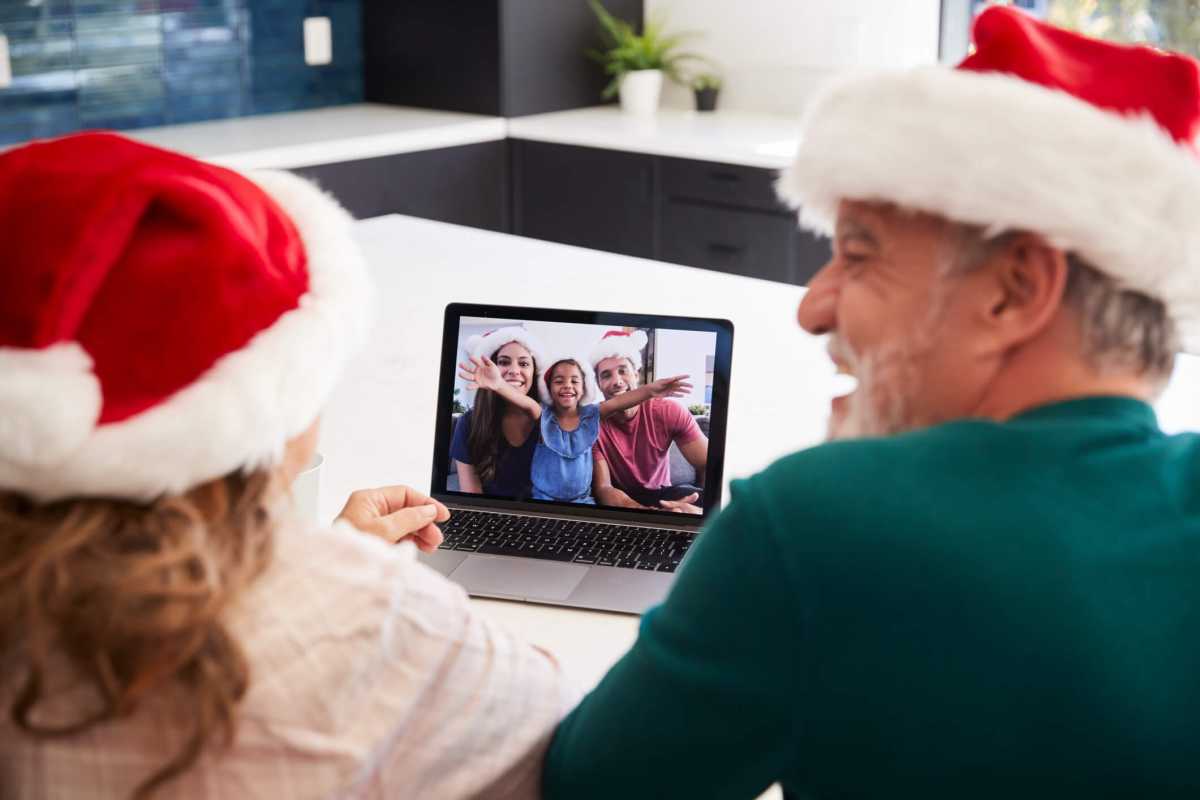 Multi-Generation Hispanic Family Wearing Santa Hats With Laptop Having Video Chat At Christmas