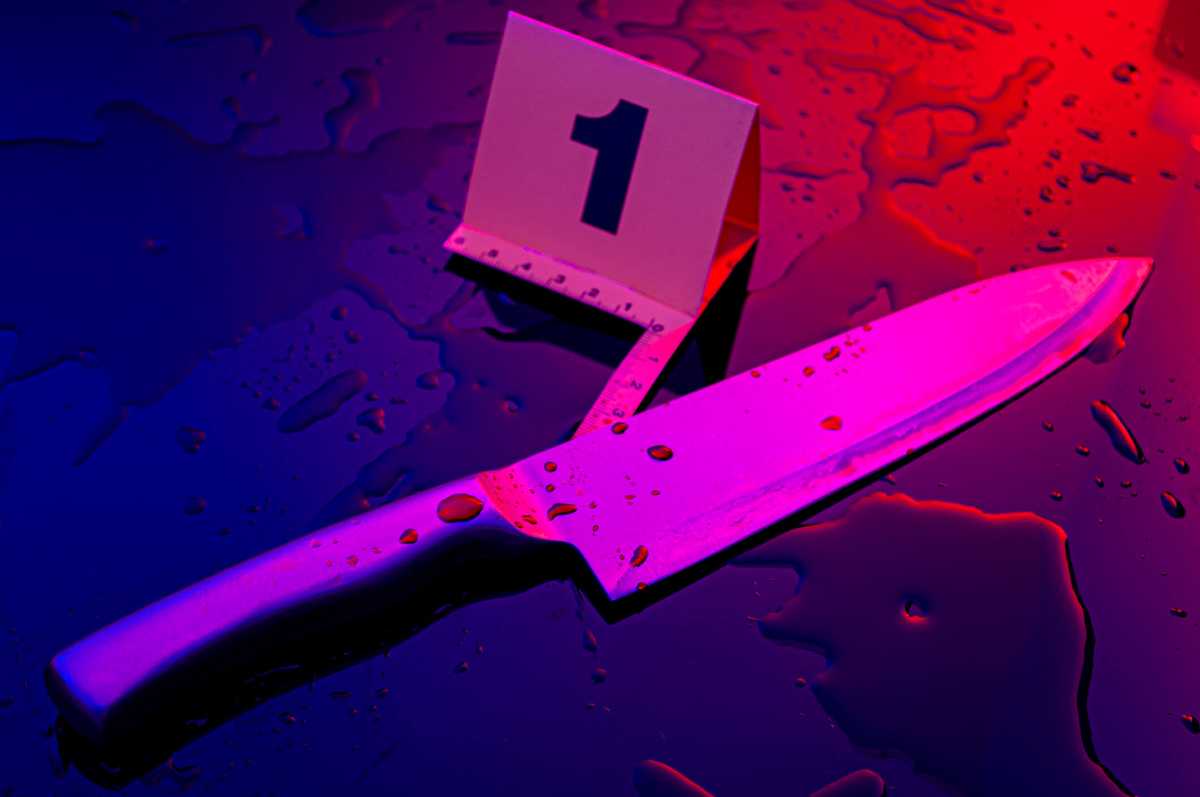 Forensic science, murder weapon and criminal investigation concept theme with kitchen knife covered in blood next to numbered marker in a dark bloody crime scene lit by cop car lights