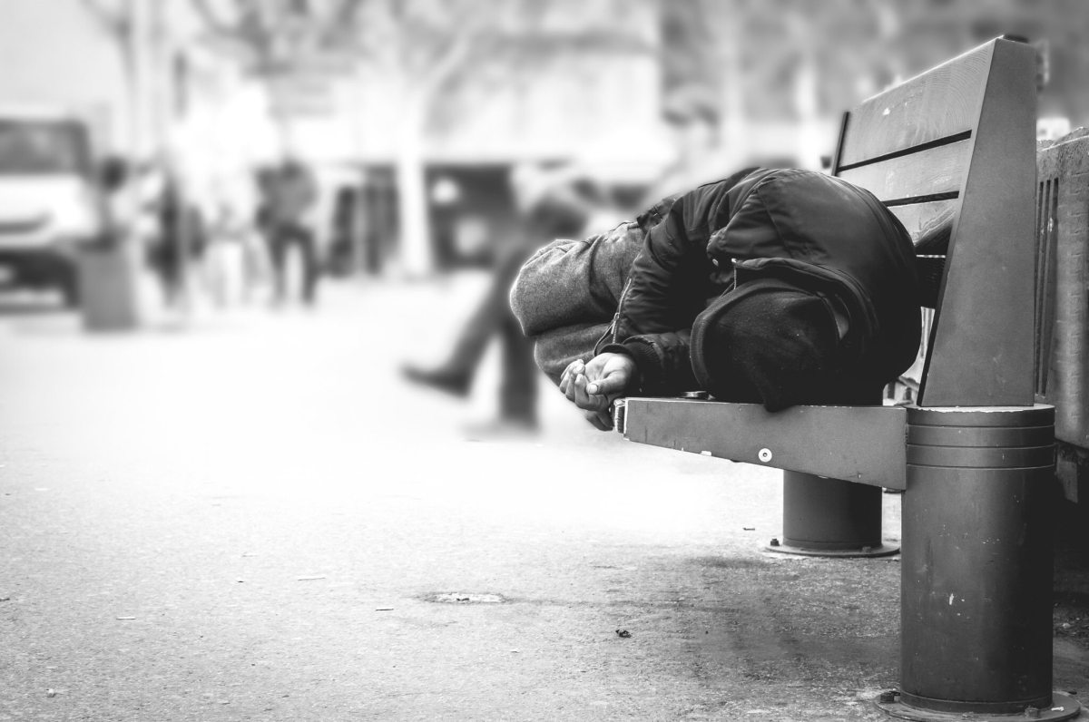 Poor homeless man or refugee sleeping on the wooden bench on the urban street in the city, social documentary concept, selective focus, black and white