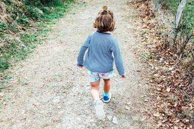 Little blond hair girl walking along a path in a forest. Nature concept