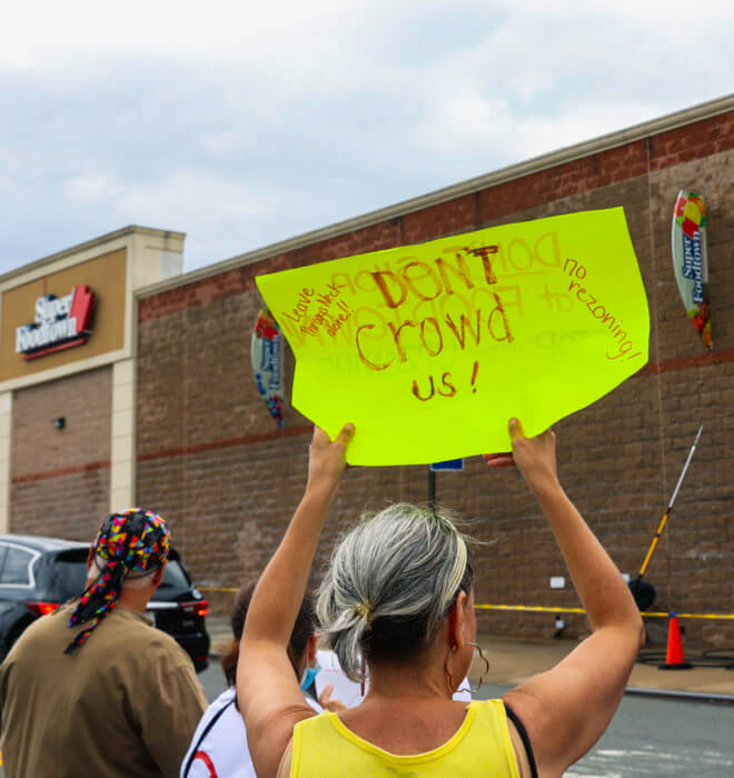 someone holds up a sign that says "Don't crowd us!" in front of the Superfood Town supermarket in August