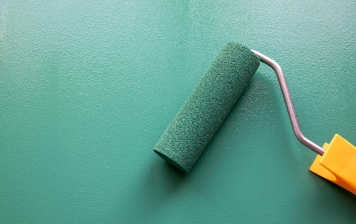 Paint roller with green colour on painted wooden surface. Chalk board