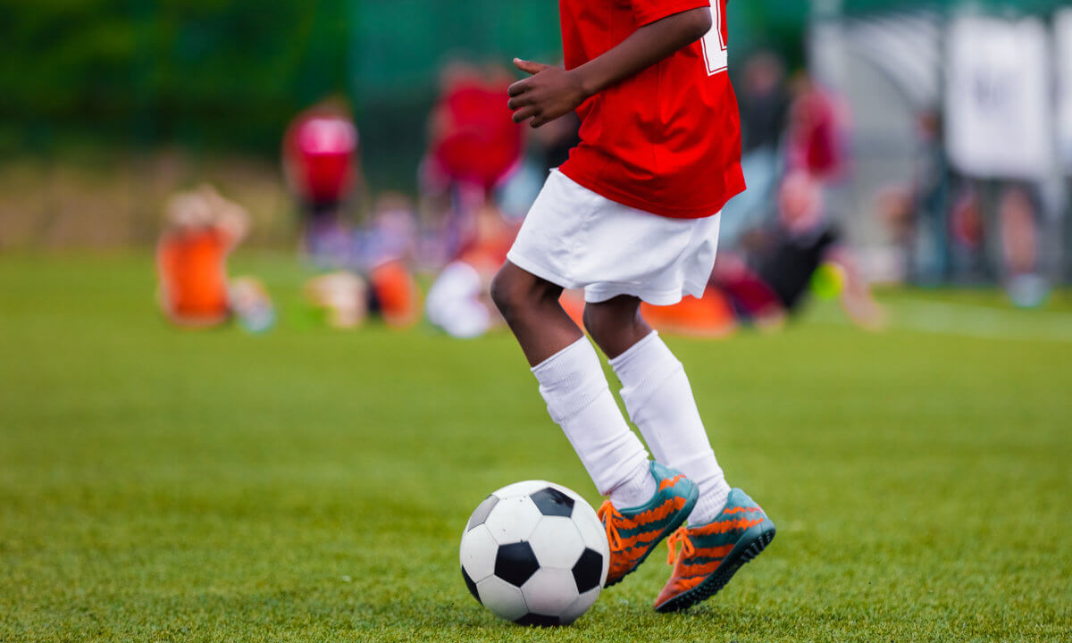African American Boy in Junior Football Team Leading Ball on Grass Training Field. Youth Soccer Player Kicking Ball