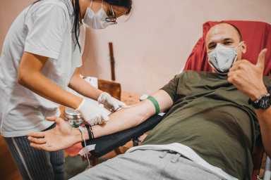 Smiling young man lying down and giving blood