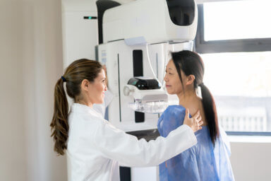 Female doctor talking to her patient and adjusting her position to do a mammogram