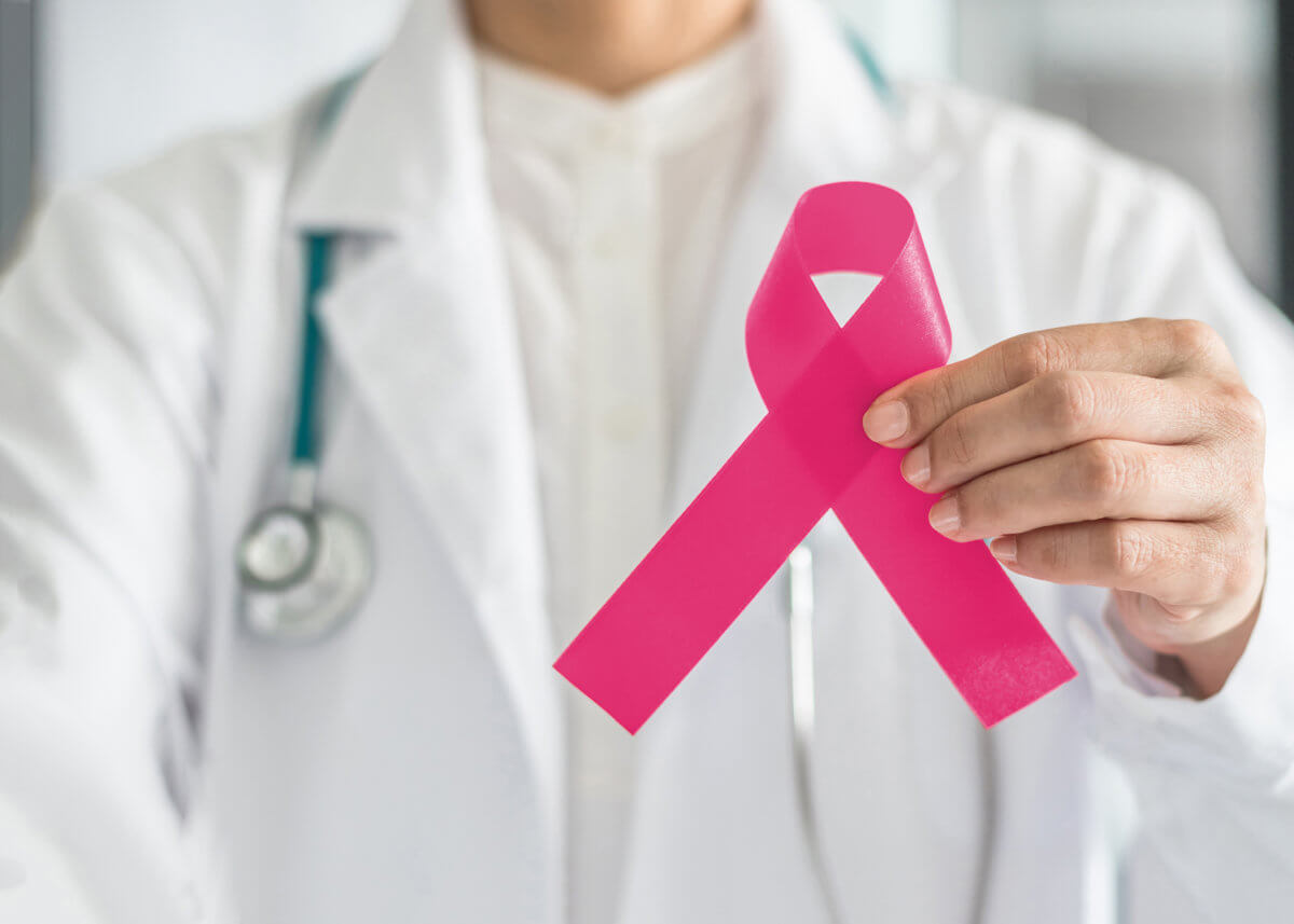 Pink ribbon for breast cancer awareness in doctor’s hand, symbolic bow color for raising awareness campaign on women (female)  patient living with breast tumor illness