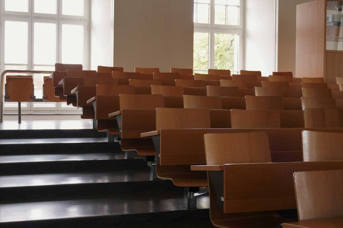 Empty auditorium at university with wooden chairs and banks and large windows and stairs on one side.