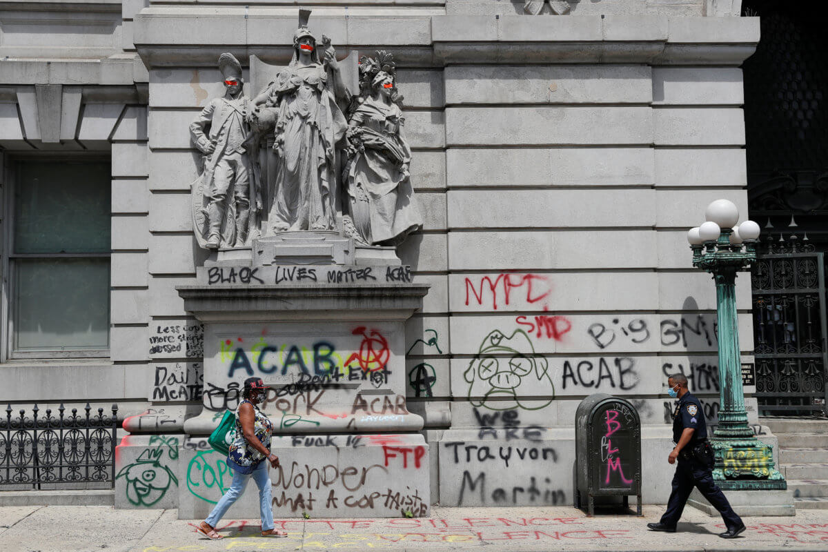 A NYPD officer and a woman walk past graffiti near the area known as the “City Hall Autonomous Zone” that has been established to protest the New York Police Department and in support of “Black Lives Matter