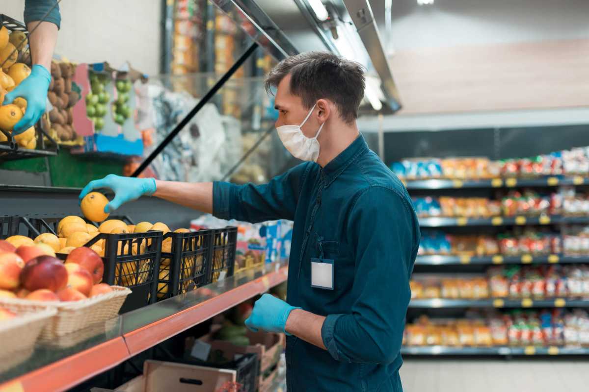 seller in a protective mask standing in front of the counter with fruit