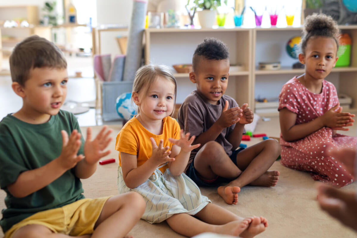 Group of small nursery school children sitting on floor indoors in classroom, clapping.