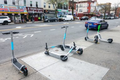 scooters parked on sidewalk, two are tipped over on the ground