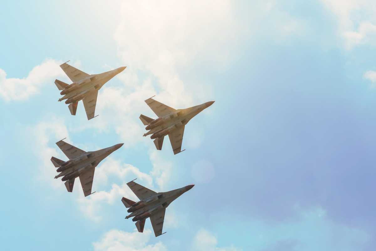 Group of four aircraft fighter jet airplane sun glow toned gradient clouds sky.