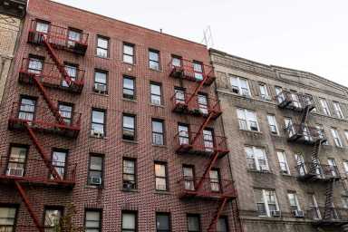 Brick apartment condo building exterior architecture in Fordham Heights center, Bronx, NYC, Manhattan, New York City with fire escapes, windows, ac units in evening
