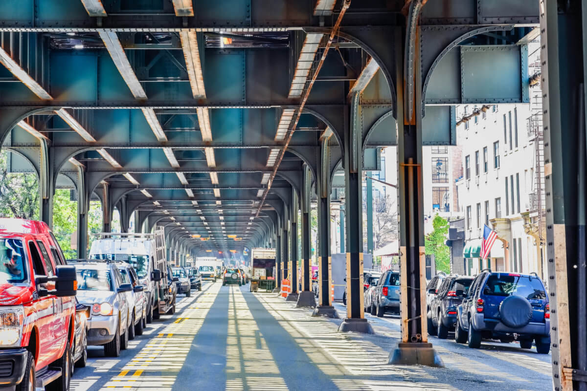 Bottom view of Elevated train track nyc. Traffic waiting in road in a sunny day. Travel and traffic concepts. Bronx, NYC, USA