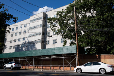a building hovering above scaffolding and a wall along a sidewalk