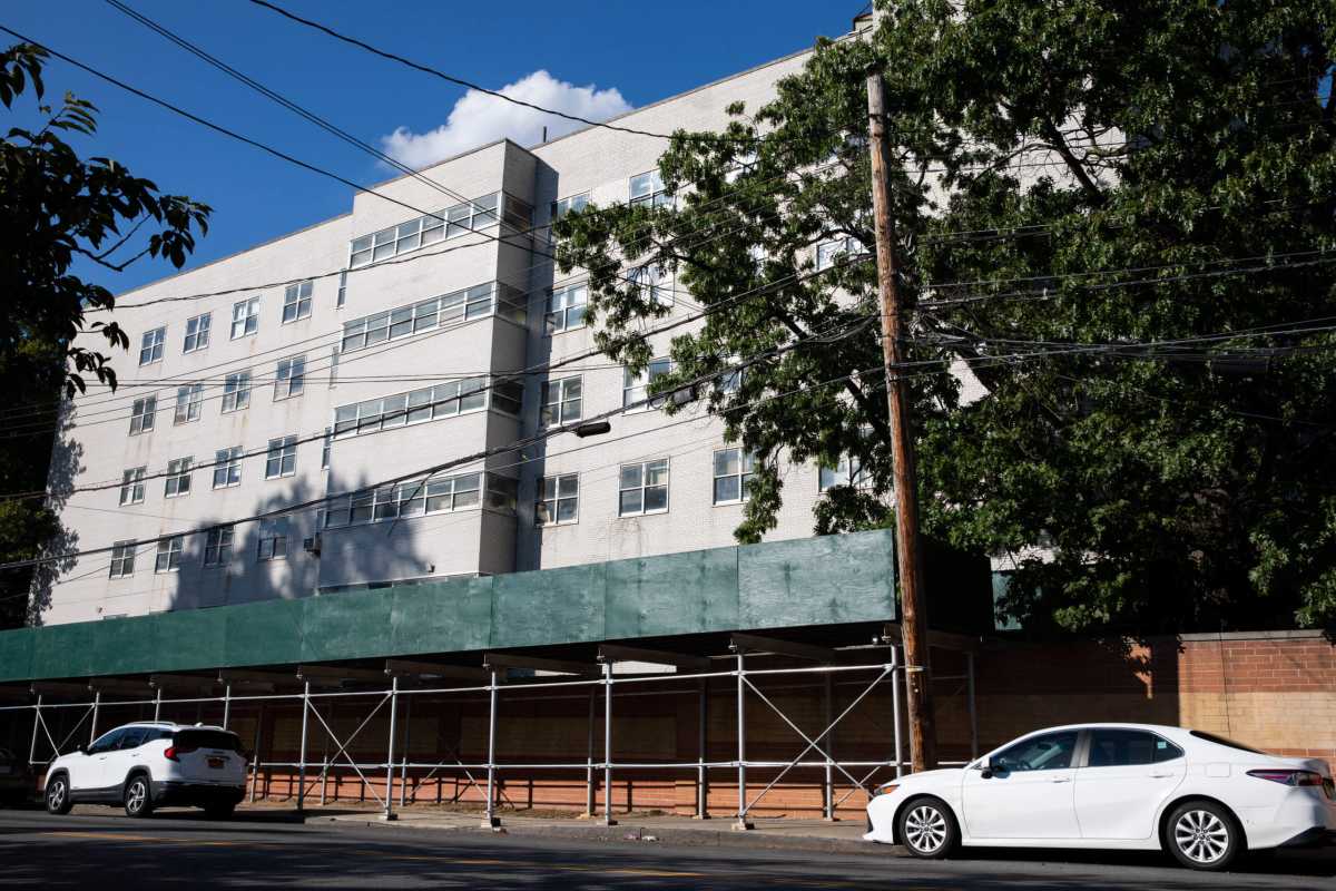 a building hovering above scaffolding and a wall along a sidewalk