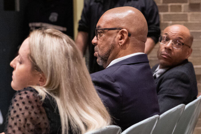 three people sitting in the public hearing audience