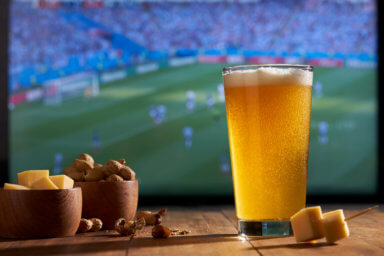 watching the soccer world cup on a large TV with a glass of beer, peanuts and cheese