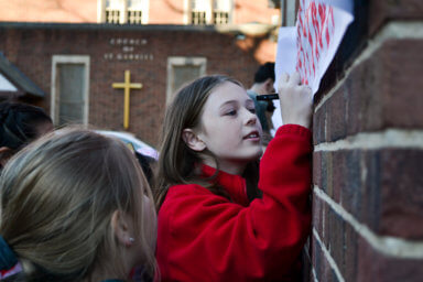 Students sign their names onto a banner with the writing “SGS Strong” painted in red on Tuesday, Feb. 14, 2023. The banner hangs onto a wall of St. Gabriel’s School in Riverdale during a rally to prevent the Archdiocese of New York from closing the school, which has been open since 1941.