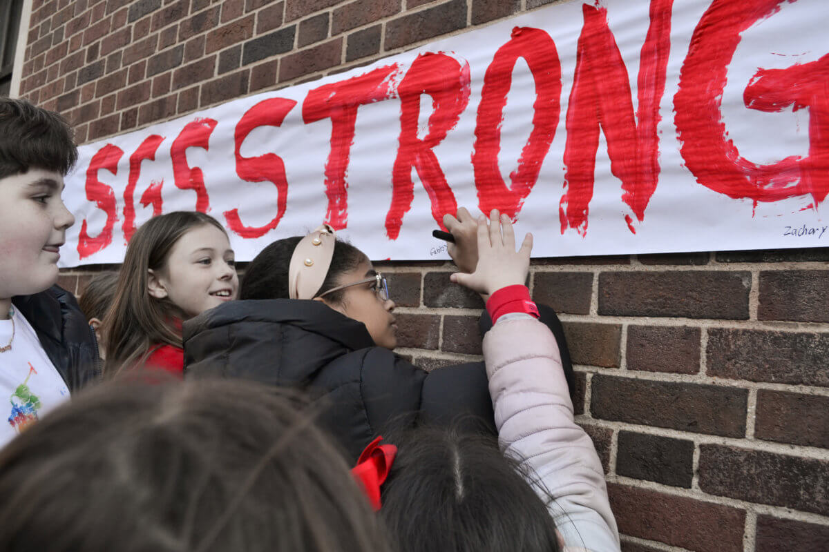 A group of students sign their names onto a banner with the writing “SGS Strong” painted in red during a rally at St. Gabriel’s School in Riverdale on Tuesday, Feb. 14, 2023.
