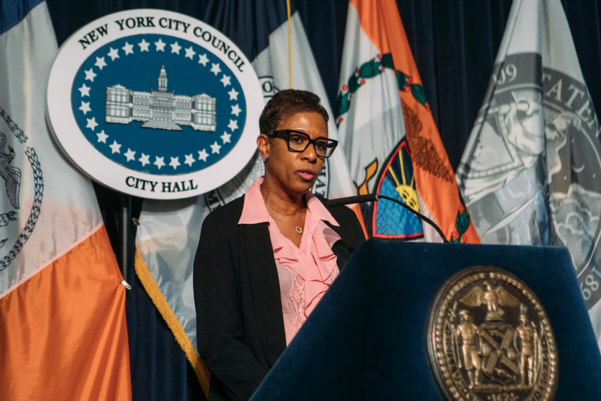 Speaker Adrienne Adams speaking into a microphone with a NYC Council City Hall sign behind her