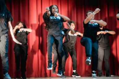 Photo of members of the Queen Crusaders step team on stage mid-performance.