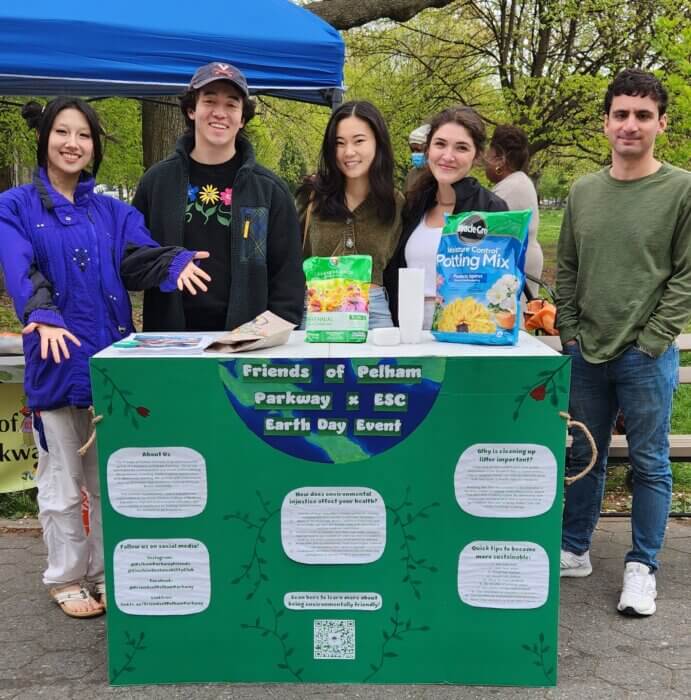Five people behind a table with a large green poster board on it, displaying information about environmental injustice.