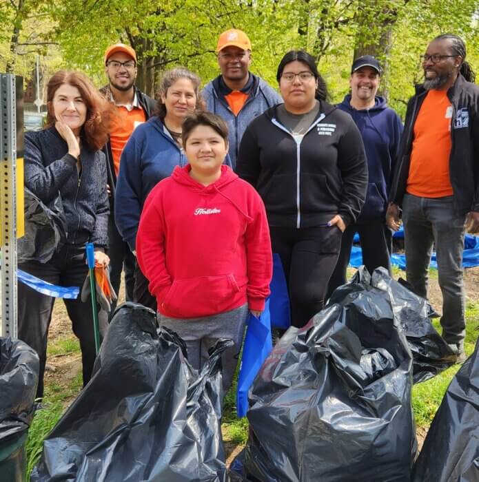 Community members of various ages and Home Depot employees standing behind bags of trash collected during Friends of Pelham Parkway's Earth Day Cleanup.