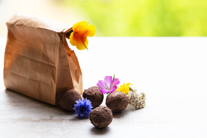 Seed bombs and flowers next to a brown paper bag on a table, blurred background.