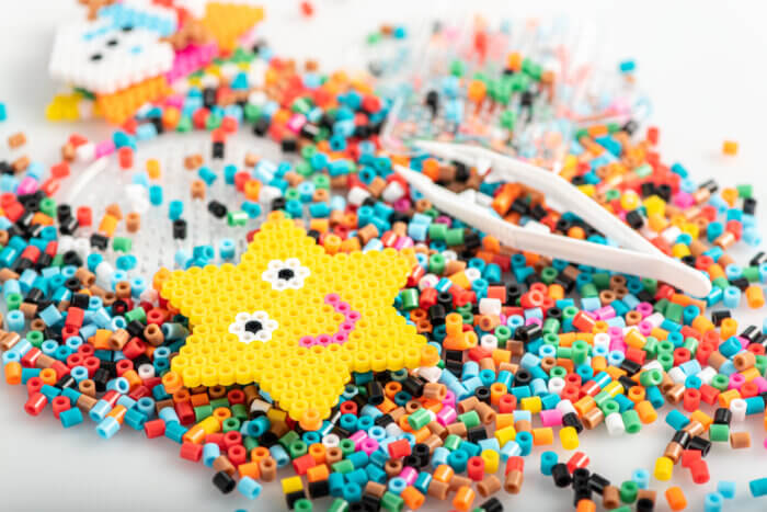 Smiling yellow star made with fusable perler beads laid atop a pile of multicolored perler beads.
