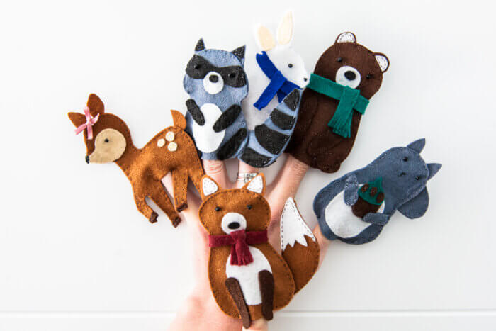 Animal felt finger puppets on someone's fingers: deer, raccoon, rabbit, bear, fox and squirrel.
