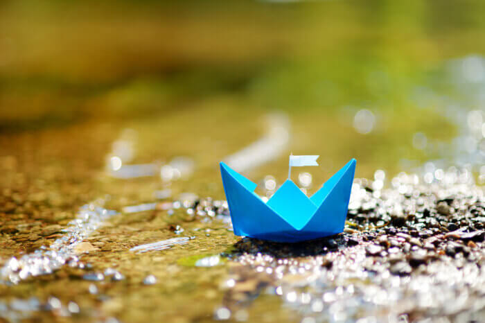 Blue paper boat with a white flag next to some running water.
