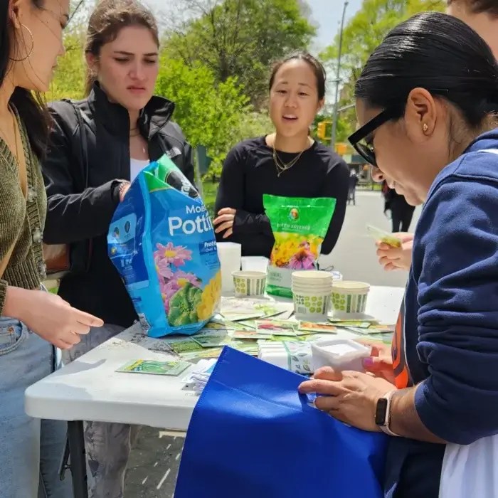 Group of people surrounding a table with small cups and a bag of potting soil on it. earth day