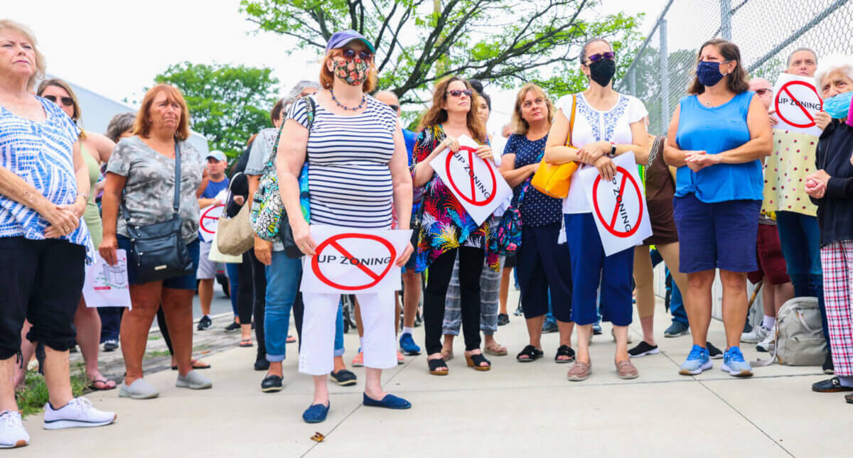 a group of people stand holding signs with the word upzoning crossed out