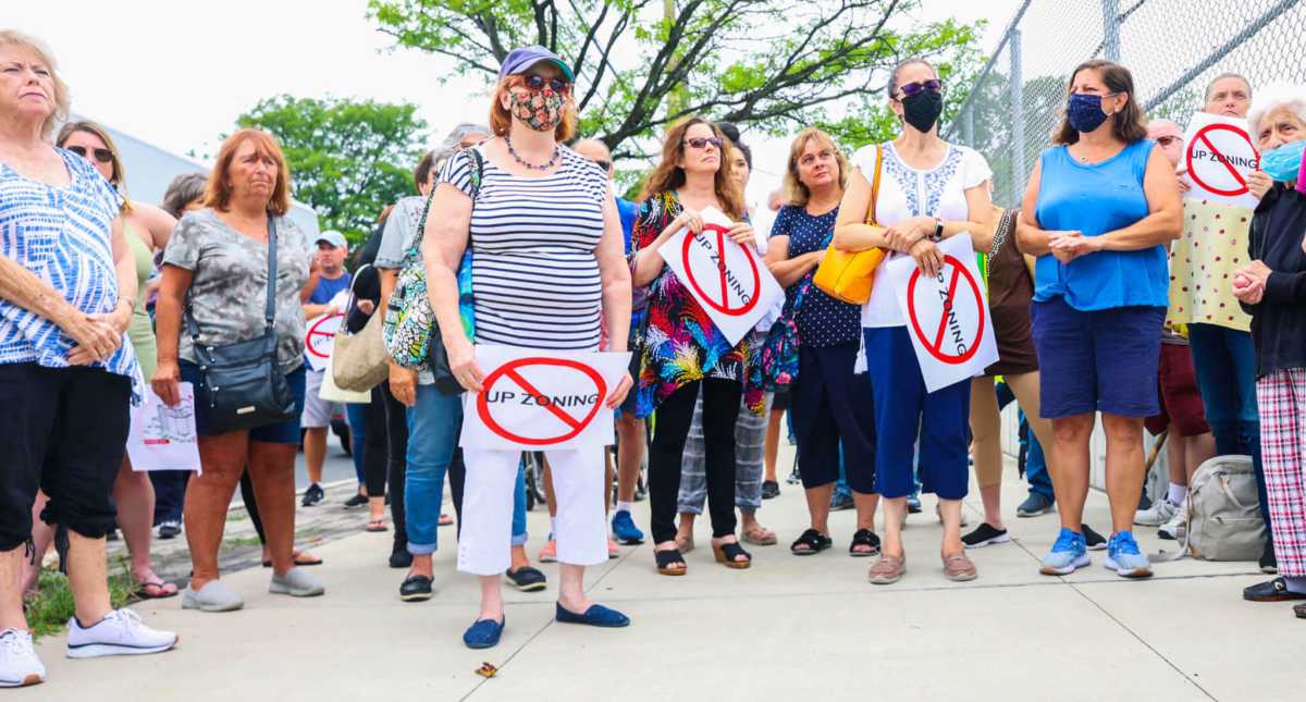 a group of people stand holding signs with the word upzoning crossed out
