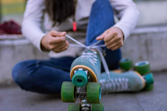 Woman sitting with head out of frame ties the laces of her roller skates