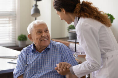 Close up caring nurse holding smiling mature patient hand