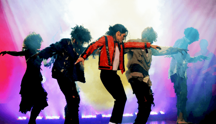 Michael Jackson impersonator dances with backround dancers and a backdrop of colorful lighting.