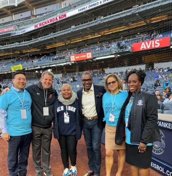 From left, NYC SBS Commissioner Kevin Kim, BOEDC President Robert Walsh, The Bronx Community Foundation CEO Meisha Porter, The NY Yankees Senior Vice President for Community Relations Brian Smith, The Bronx Chamber of Commerce President Lisa Sorin and Bronx Borough President Vanessa Gibson stand with their arms around each other at Yankee Stadium.