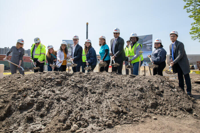 A group of people hold shovels over a pile of dirt