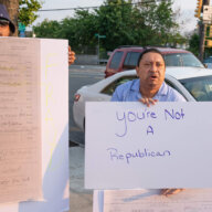 two protestors hold signs. one sign is a picture of a petition and the other sign says "You're not a Republican"