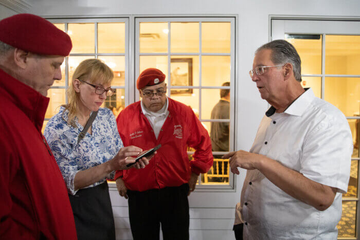 Curtis Sliwa, Nancy Sliwa and Arnaldo Salinas look at a phone in Nancy's hand and George speaks to them 