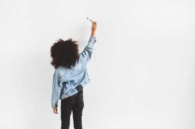 A dark-skinned girl stands near the wall and writes something.