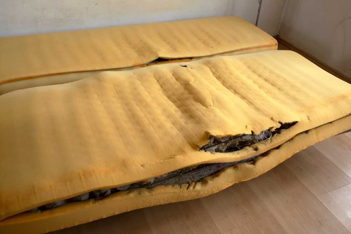 An old tattered foam mattress with protruding springs in a room with dirty walls. Poverty, disorder