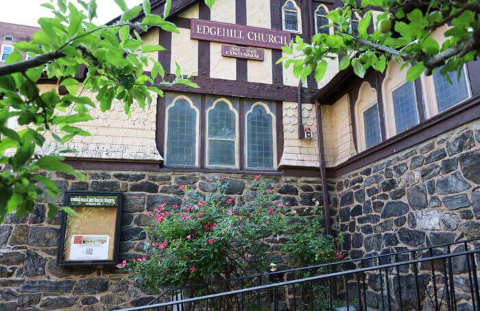 picture shows an Edgehill Church sign on the side of the building, as well as tree branches and flowers around the building
