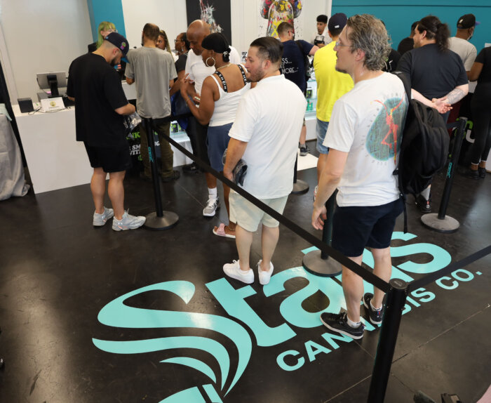 people stand on line in the dispensary, standing on top of a Statis Cannabis Co. decal on the floor