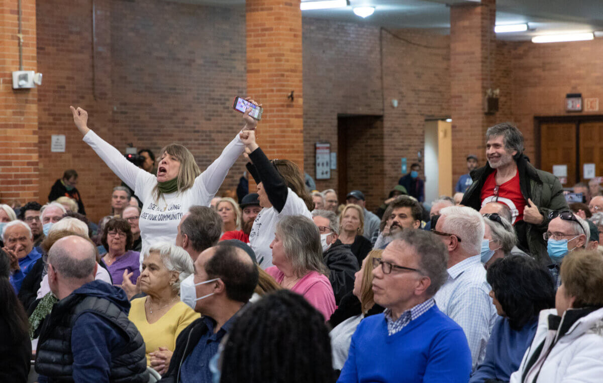 meeting attendees stand up with their arms up at a rowdy meeting about the Bruckner rezoning